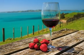 A Glass of Red Wine with Strawberry Standing on Old Table at the Beach on the Pacific Coast, Auckland, New Zealand